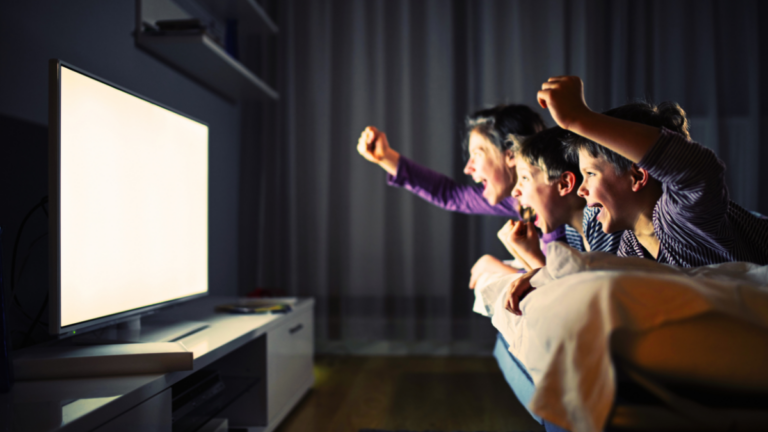 A mom and 2 kids watching TV in the dark cheer on pop icons in the autism community