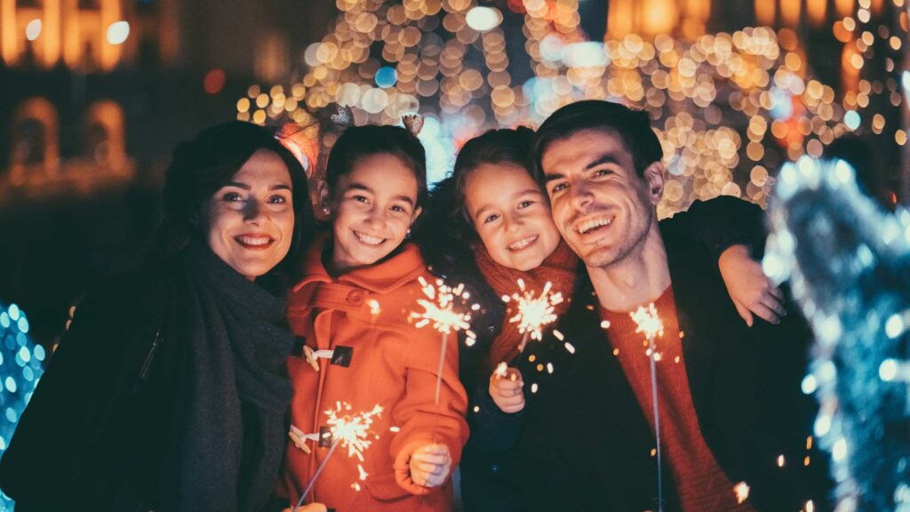 A family sharing a joyful, sensory‑friendly holiday evening, holding small sparklers with soft glowing decorations behind them
