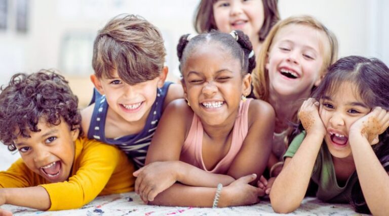 Group of smiling young children lying together on the floor, representing community and inclusion in a blog about autism safety tips and practical safety strategies for families