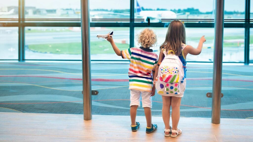 Kids with backpacks looking out at airplanes through large airport windows illustrating autism and airplanes