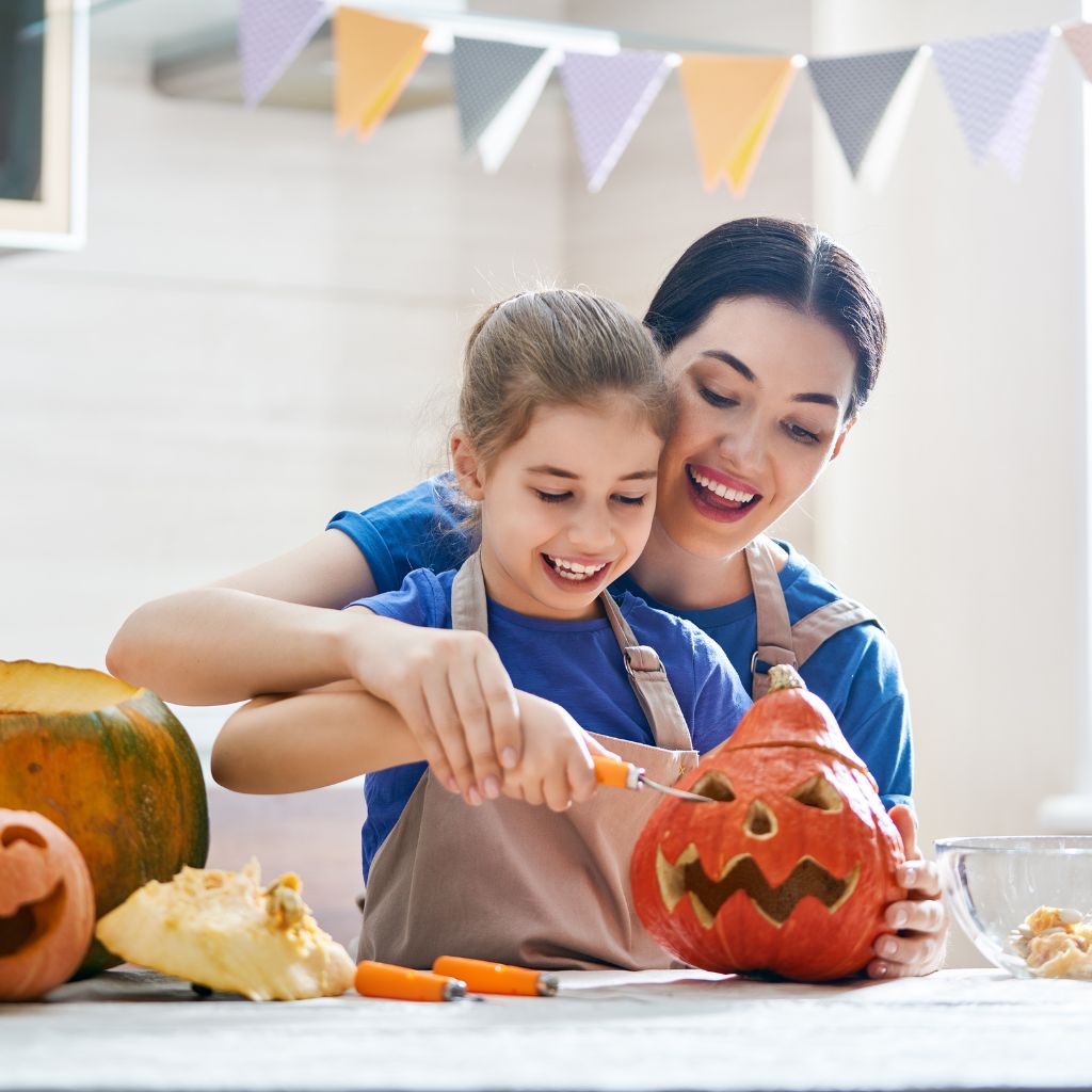 Mother helping her daughter carve a pumpkin as part of a sensory-friendly Halloween activity at home.