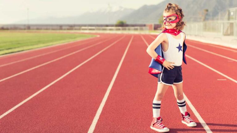 Young child in superhero costume standing confidently on a running track, representing self-advocacy skills and autism self-advocacy