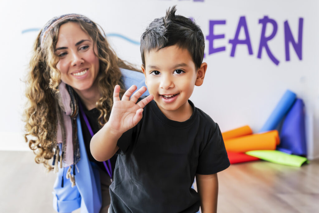aba therapy for toddlers Child waving during ABA therapy for toddlers with therapist nearby