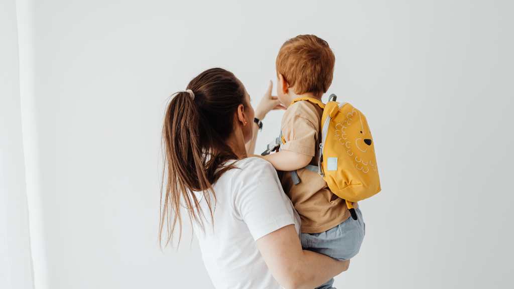 Mother holding toddler with backpack, early signs of autism at 18 months and developmental milestones