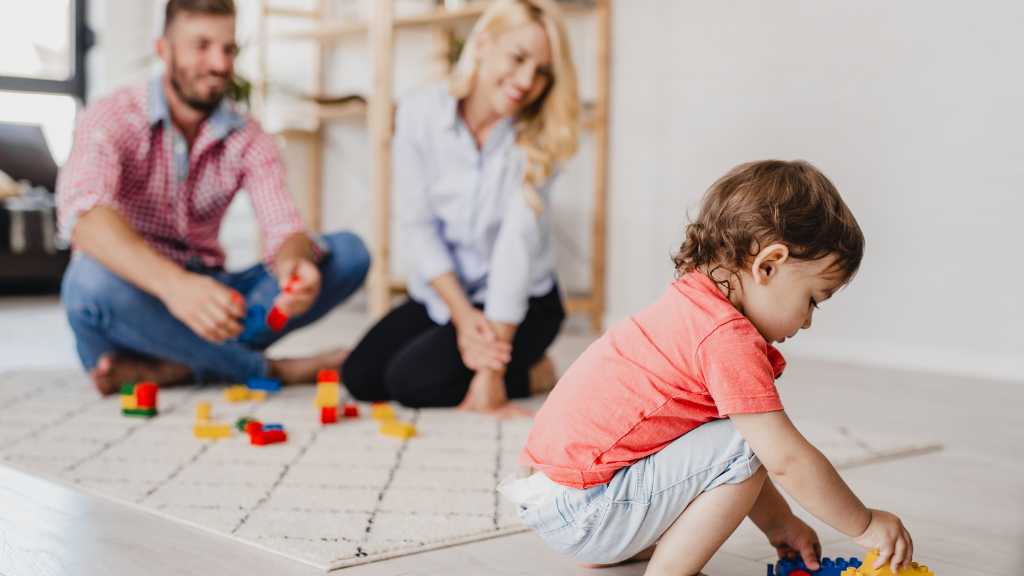 Toddler playing alone while parents watch, illustrating autism signs in infants